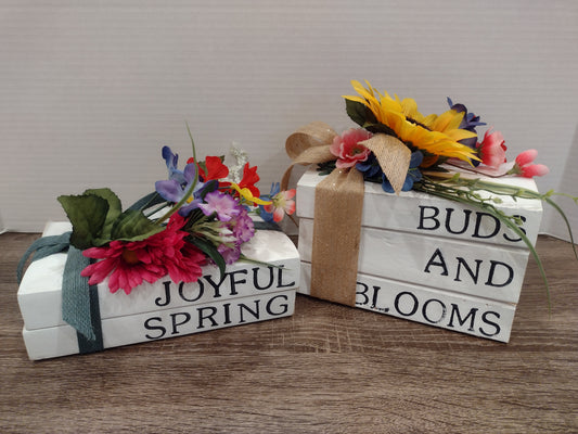 Two decorative books with floral arrangements and text on a surface.